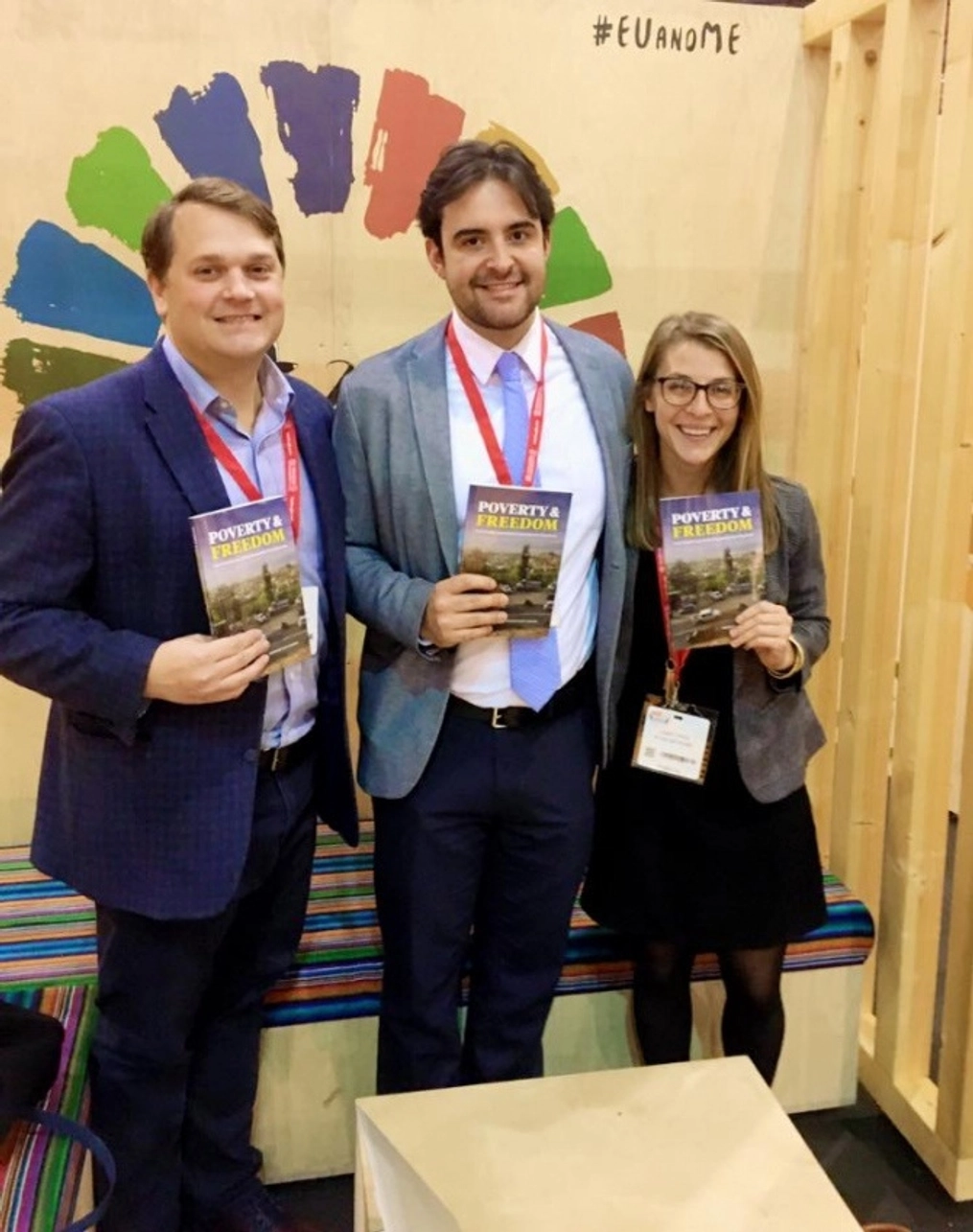 Two men and a woman hold copies of Poverty & Freedom.