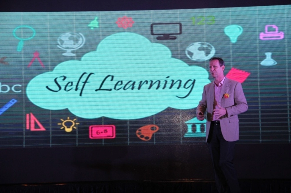 A man stands before a large graphic with text that says "Self Learning."