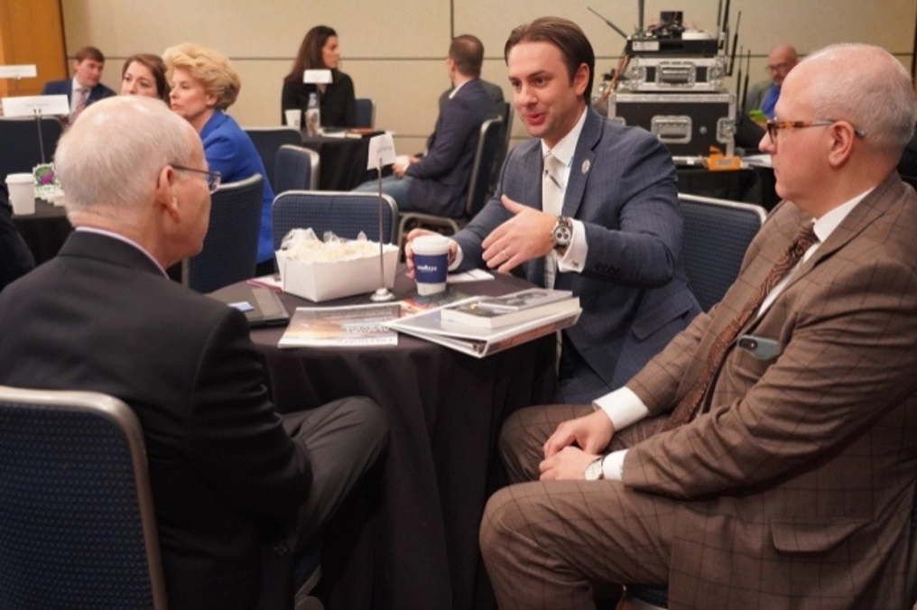 Three men in conversation at a small table.