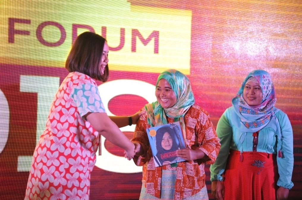 Three women stand on stage as one congratulates another.