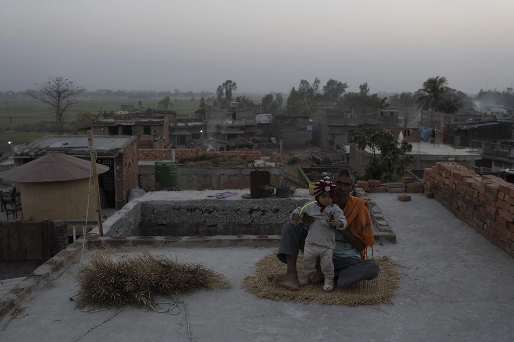 A child sits with a man on a rooftop in Sugauli Birta, an agrarian community near the Indian border of Nepal.