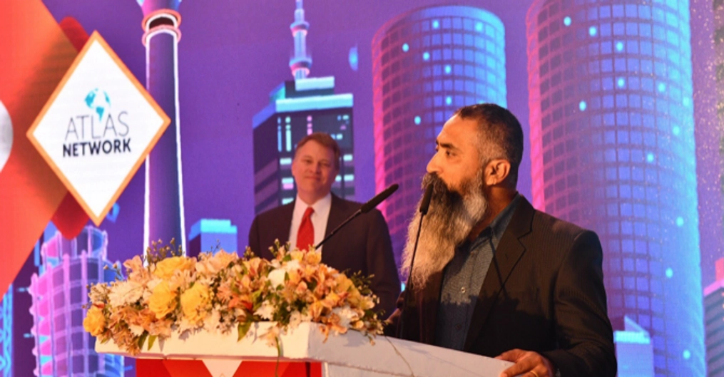 Adhikari on stage delivering a speech as Brad Lips watches.