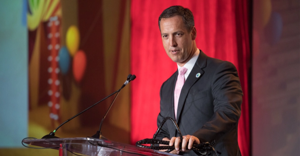 A man wearing a suit delivers a speech from a podium onstage.