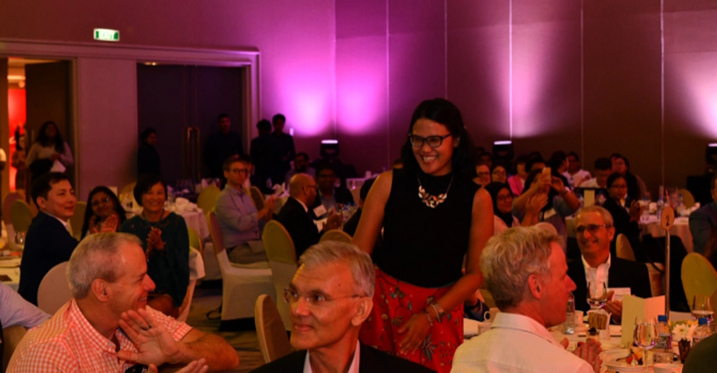 Haryoko stands among a seated crowd at banquet tables.